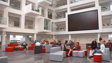 Students-sit-talking-under-AV-screen-in-atrium-at-university