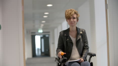 Female-student-in-wheelchair-moves-into-focus-in-a-corridor