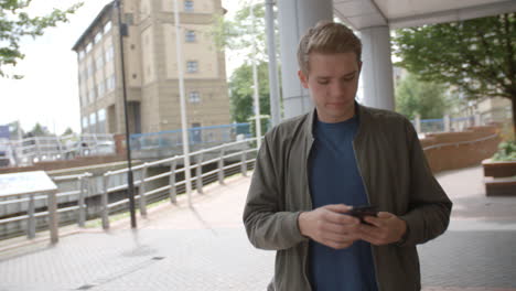 Young-white-man-walking-in-urban-setting-answering-his-phone