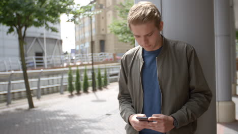 Junger-Weißer-Mann,-Der-Im-Städtischen-Umfeld-Nachrichten-Mit-Dem-Smartphone-Sendet