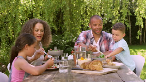 Family-At-Home-Eating-Outdoor-Meal-In-Garden-Together