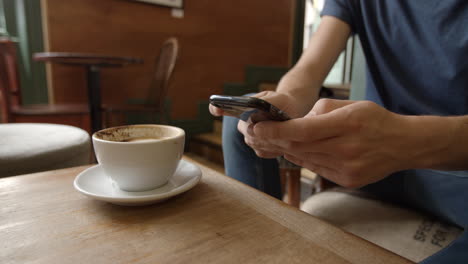Man-in-cafe-using-phone-and-drinking-coffee,-close-up-detail