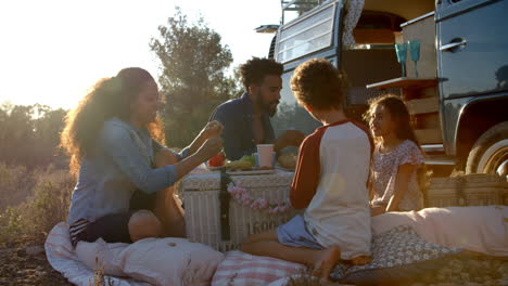 Family-eating-picnic-outside-their-camper-van-at-sundown