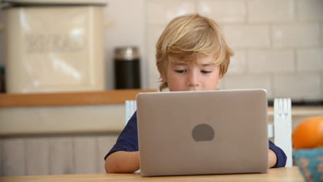 Young-boy-using-laptop-computer-at-kitchen-table,-close-up