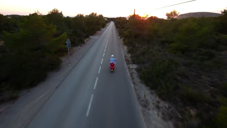 Drone-shot-following-a-scooter-on-a-road-through-trees