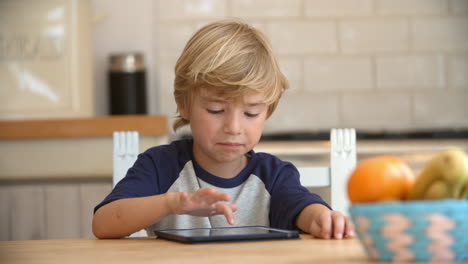 Young-boy-using-tablet-computer-at-kitchen-table,-pan
