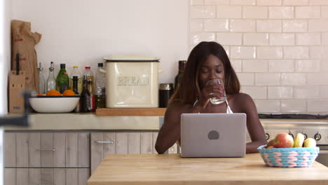 Smiling-young-woman-using-laptop-computer-in-her-kitchen,-shot-on-R3D