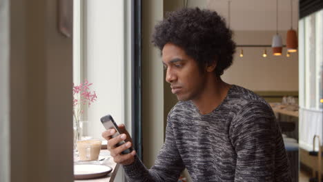 Young-Man-Using-Mobile-Phone-To-Update-Social-Media-In-Cafe