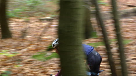 Young-man-cross-country-cycling-between-trees-in-a-forest,-shot-on-R3D