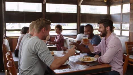 Four-male-friends-making-a-toast-at-a-table-in-a-restaurant,-shot-on-R3D