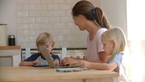 Mum-and-kids-using-computers-and-drawing-at-kitchen-table