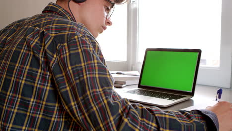 Teenage-boy-wearing-headphones-writing-at-desk-in-his-bedroom,-shot-on-R3D