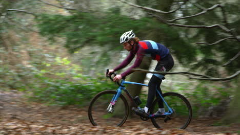Young-man-cross-country-cycling-between-trees-in-a-forest,-shot-on-R3D