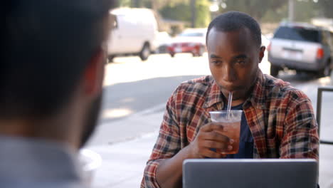 Two-male-friends-with-cold-drinks-and-laptop-outside-coffee-shop
