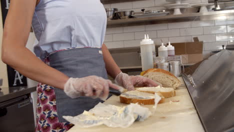 Woman-buttering-bread-at-a-sandwich-bar,-mid-section