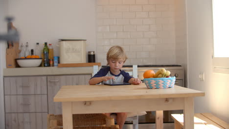 Young-boy-using-tablet-computer-in-kitchen,-from-doorway