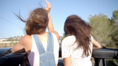 Two-female-friends-standing-up-in-the-back-of-a-moving-car