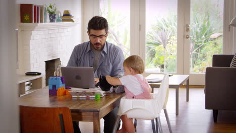 Vater-Arbeitet-Von-Zu-Hause-Aus-Am-Laptop,-Während-Sein-Sohn-Mit-Spielzeug-Spielt