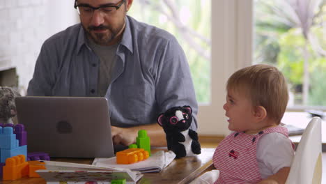 Father-Working-From-Home-On-Laptop-As-Son-Plays-With-Toys