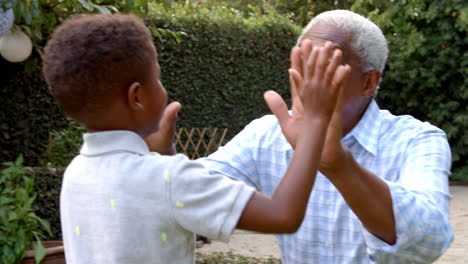 Young-black-boy-playing-clapping-game-with-grandad-in-garden