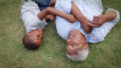 Black-grandad-and-grandson-play-lying-on-grass,-aerial-view