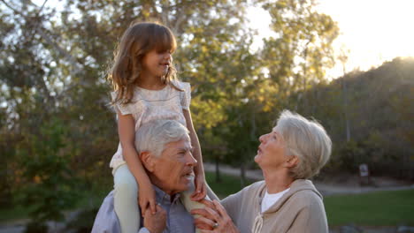 Grandparents-Giving-Granddaughter-A-Shoulder-Ride-In-Park