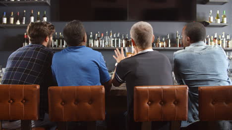 Rear-View-Of-Male-Friends-Watching-Game-In-Sports-Bar