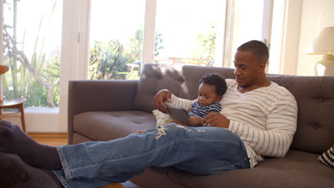 Vater-Und-Sohn-Sitzen-Zu-Hause-Auf-Dem-Sofa-Und-Nutzen-Ein-Digitales-Tablet