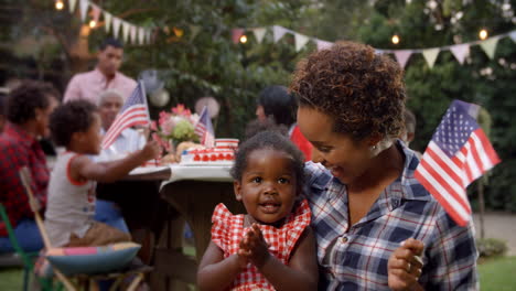 Black-mother-and-baby-girl-wave-flag-at-4th-July-party