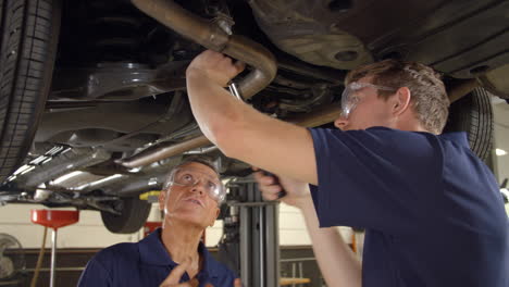 Mechanic-And-Male-Trainee-Working-Underneath-Car-Together