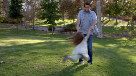 Father-Swinging-Daughter-By-Her-Arms-In-Park