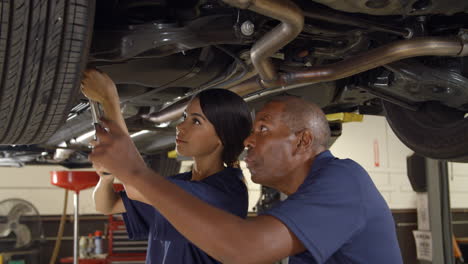 Mechanic-And-Female-Trainee-Working-Underneath-Car-Together