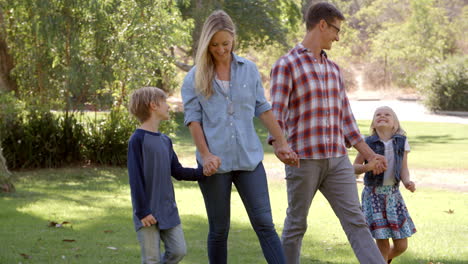 Young-family-walk-holding-hands-in-a-park-in-the-sun,-pan