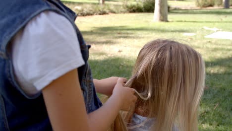 Young-daughter-braiding-mother's-hair-in-a-park