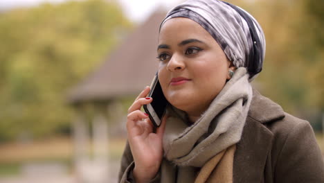Mujer-Musulmana-Británica-Usando-Teléfono-Móvil-En-El-Parque