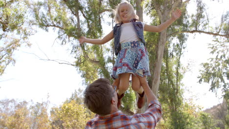 Dad-holding-his-young-daughter-in-the-air-in-a-park