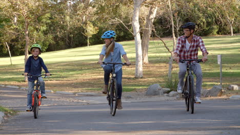 Parents-and-son-cycling-towards-camera-in-a-park