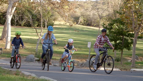 Panning-shot-following-family-cycling-together-in-a-park