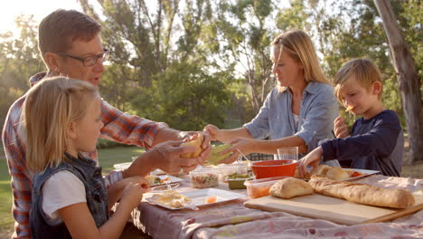 Young-white-family-enjoying-a-picnic-at-a-table-in-a-park