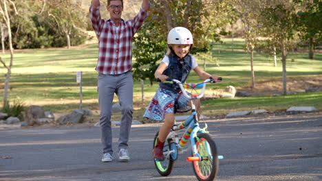 Father-teaching-his-daughter-to-ride-a-bike-in-a-park