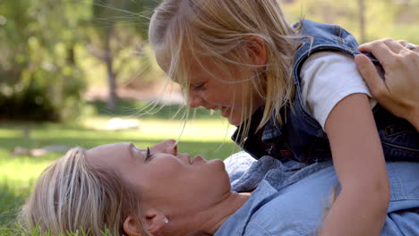 Young-daughter-lying-on-her-mother-in-a-park,-close-up