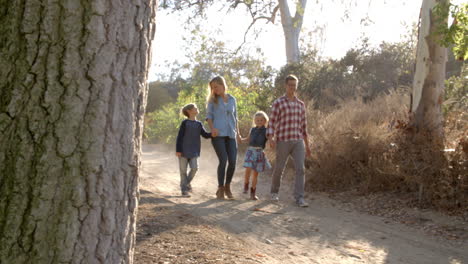 Young-white-family-walking-on-a-path-in-sunlight,-front-view