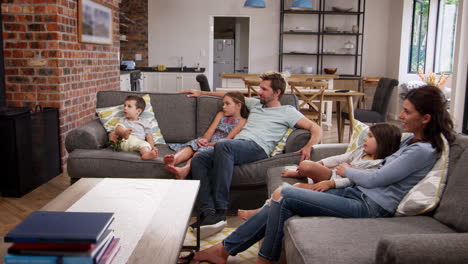 Family-Sit-On-Sofa-In-Open-Plan-Lounge-Watching-Television