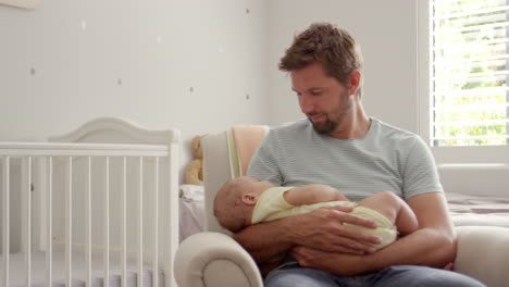 Father-Sitting-In-Nursery-Chair-Holds-Sleeping-Baby-Son