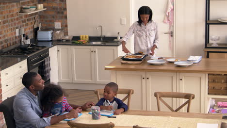 Vater-Und-Kinder-Zeichnen-Am-Tisch,-Während-Die-Mutter-Das-Essen-Zubereitet
