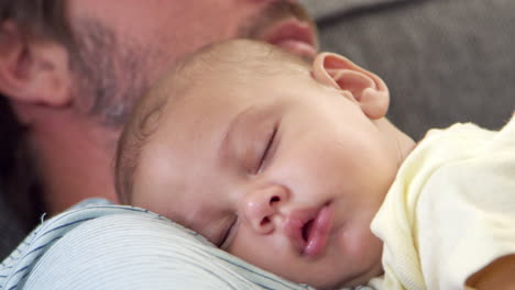 Close-Up-Of-Father-Sitting-On-Sofa-Holding-Sleeping-Baby-Son