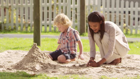 Teacher-At-Montessori-School-Playing-With-Male-Pupil-In-Sand-Pit