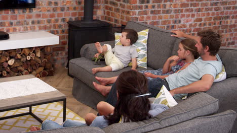 Family-Sit-On-Sofa-In-Open-Plan-Lounge-Watching-Television