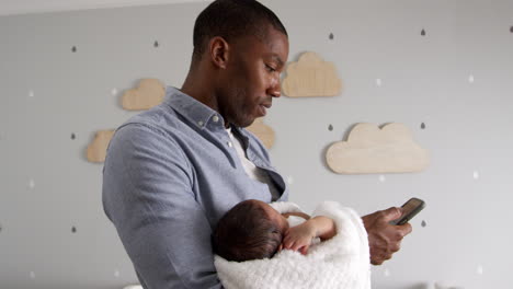 Father-Holding-Newborn-Baby-Son-Using-Mobile-Phone