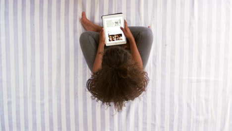 Overhead-View-Of-Teenage-Girl-Looking-At-Digital-Tablet-On-Bed